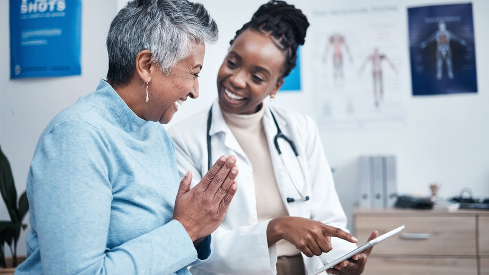 Healthcare provider points at tablet while speaking with elderly patient, both smiling in an exam room.
