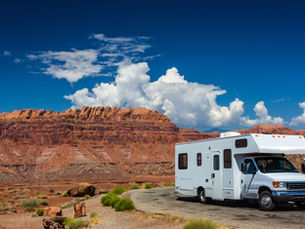 An RV parked on the side of a road next to a stretch of desert. There are raised plateaus in the distance.