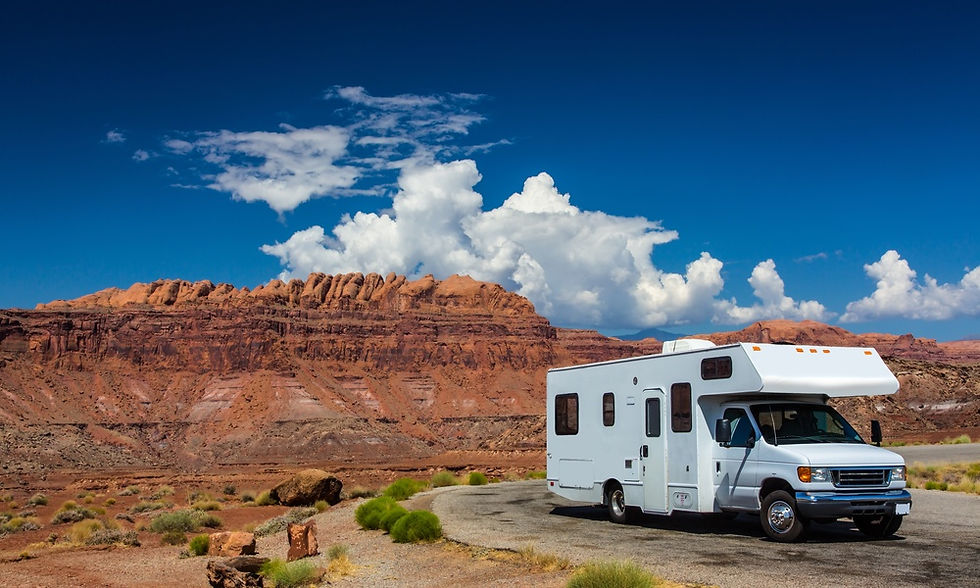 An RV parked on the side of a road next to a stretch of desert. There are raised plateaus in the distance.