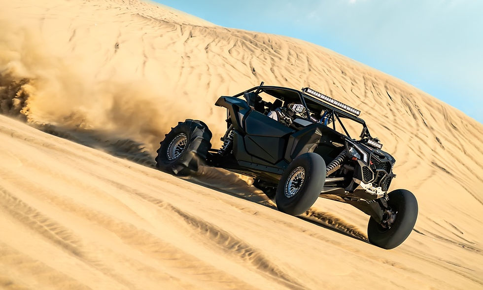 An off-roading UTV driving through the sand of a desert. The wheels of the vehicle are kicking up clouds of sand.