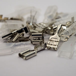 A pile of automotive connectors on a table. Some connectors are metal and some are made from a translucent plastic.
