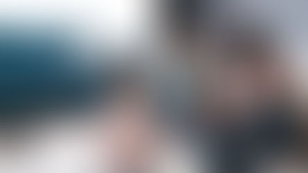 A couple with a child are sitting on the ground in a living room. The adults are both smiling but the child is turned away from the camera.