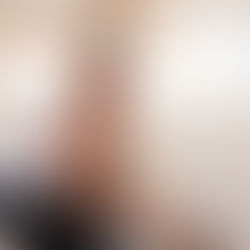 A couple repainting a room in a home with white walls, carpet, and a window on the back wall letting light in.