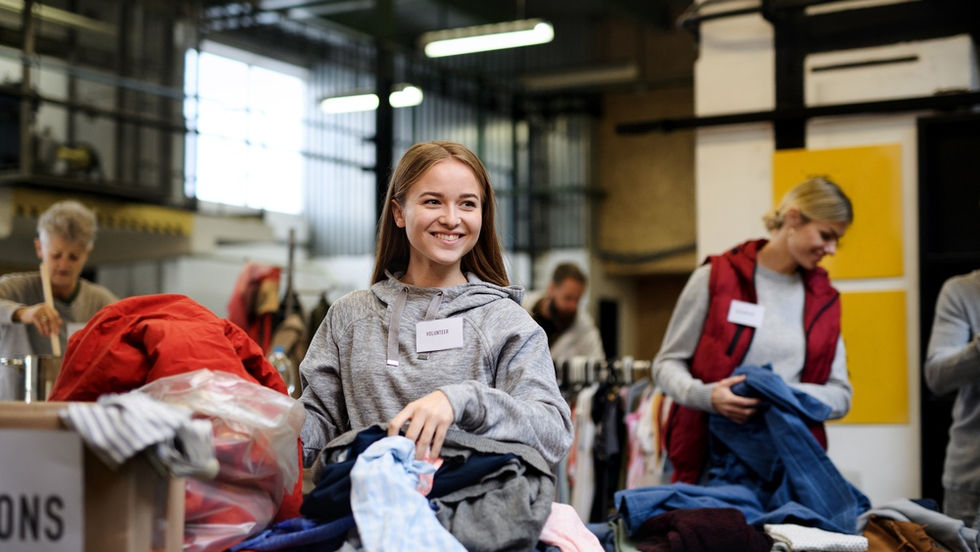 A close-up of a young woman sorting through a stack of clothing with other volunteers at a donation center.