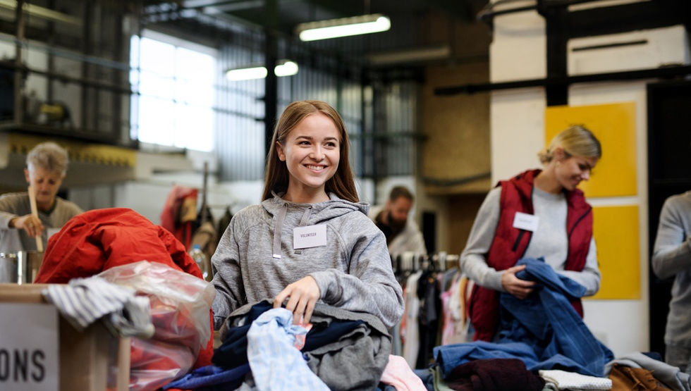 A close-up of a young woman sorting through a stack of clothing with other volunteers at a donation center.
