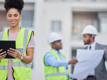 Smiling site supervisor in high-visibility vest holds a tablet; two hard-hat coworkers review plans behind.