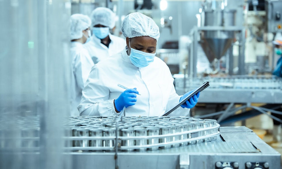 Worker in protective gear inspects cans on a food processing line as colleagues and industrial machinery fill the background.