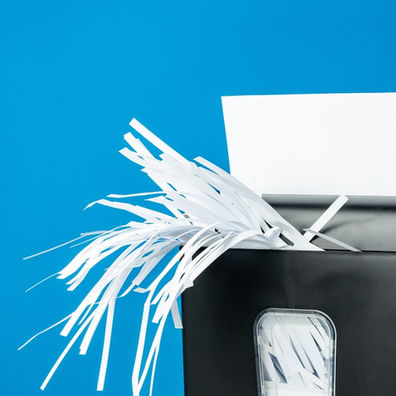 Black paper shredder cuts a white sheet into long strips, with shredded paper spilling out against a blue background.