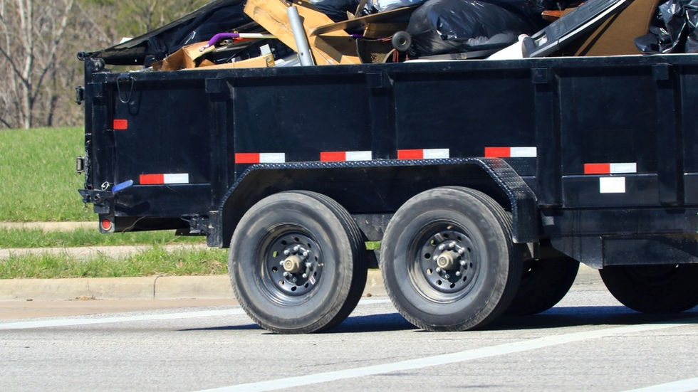 A small open trailer loaded with black garbage bags and loose refuse, parked on an asphalt road outdoors.