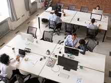 An overhead view of employees working at shared desks in a modern open office with desktop computers.