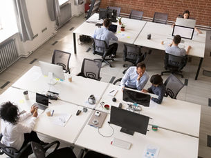 An overhead view of employees working at shared desks in a modern open office with desktop computers.