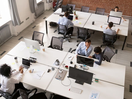 An overhead view of employees working at shared desks in a modern open office with desktop computers.