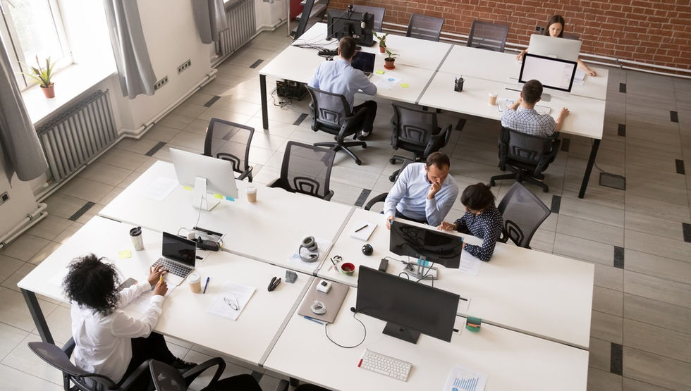 An overhead view of employees working at shared desks in a modern open office with desktop computers.