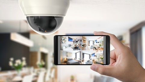 A close-up of a hand holding up a smartphone with views from four home security cameras next to a ceiling-mounted camera.