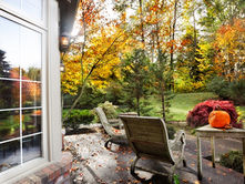 Two chairs and a small table on a backyard patio covered in fallen leaves. A pumpkin sits on the table.