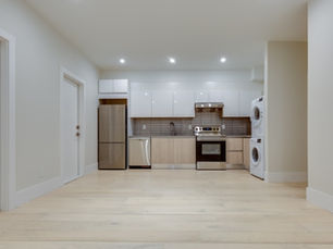 A bright basement apartment contains a modern kitchen, pale wood floors, and a stacked washer and dryer.