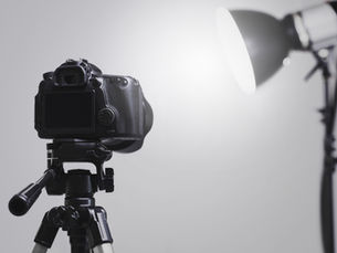 Camera on a tripod facing a bright studio light against a gray background, creating a professional photography setup.