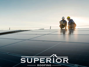 Two roof workers in hard hats inspect solar panels at sunset, one using a laptop; SUPERIOR ROOFING text below.