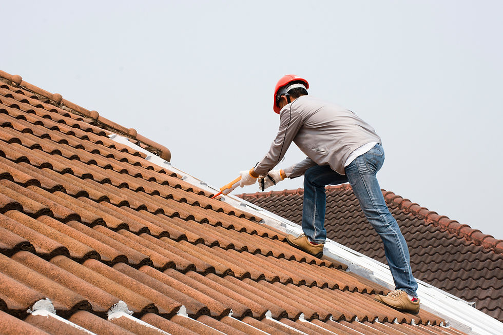 Worker in red helmet applies sealant on brown tiled roof. Clear sky background. Safety gear visible. Focused and careful mood.