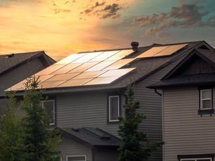 Suburban house roofs covered with solar panels glowing at sunset under a warm orange sky.