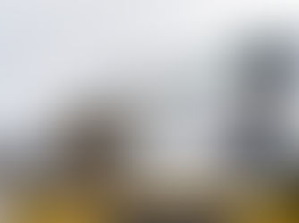 Three workers install roofing shingles on a house. They wear safety gear and use tools. The sky is overcast, creating a focused mood.