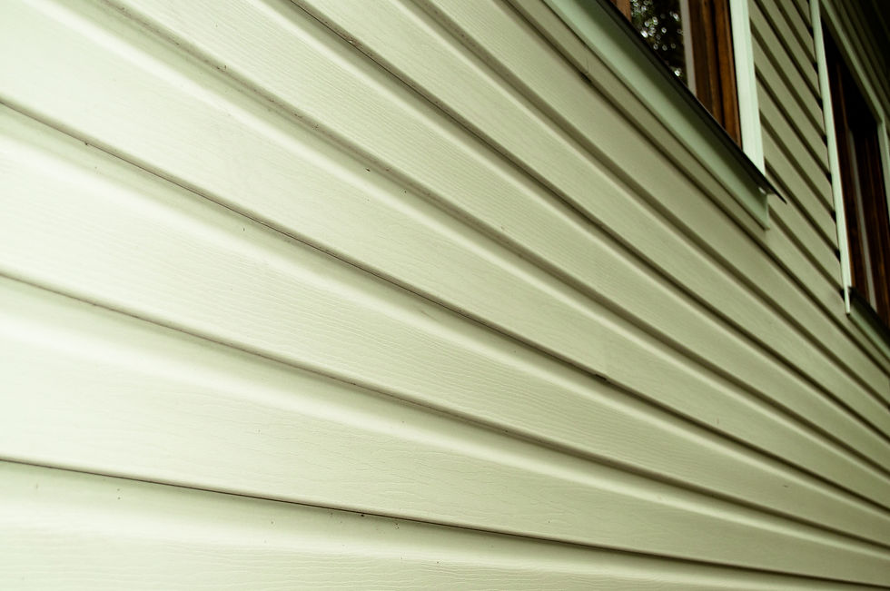 Close-up of beige house siding with strong diagonal lines, sunlight casting shadows, and a window visible at the top right.