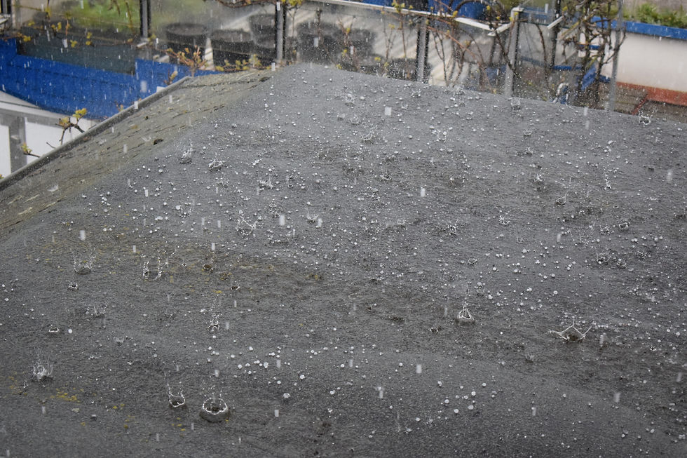 Hail pelts a dark rooftop, with white pellets bouncing in a gray stormy scene and buildings blurred in back.