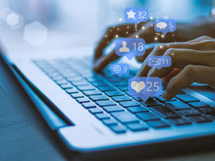 ands typing on a laptop keyboard with floating social media icons showing numbers: 32 stars, 18 people, 9 emails, 25 likes, 5 comments.