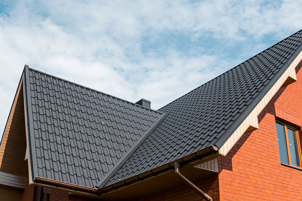 Gabled roof with dark shingles on a red brick building against a blue sky with clouds. Brown gutters run along the roof edges.
