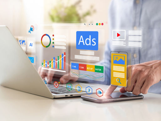 Person using a laptop and smartphone with digital ads, graphs, and icons floating in the air. Bright, modern tech setting.
