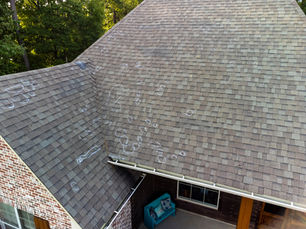 Rooftop with chalk circles indicating possible hail damage. Brown shingles are visible, with trees in the background and a blue bench below.
