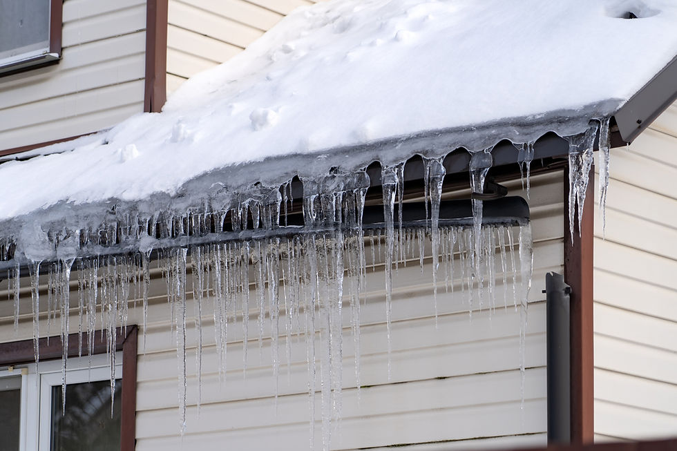 Icicles hang from a snow-covered roof of a house with white siding. The scene is crisp and wintry, conveying a cold atmosphere.