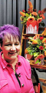 Lady with purple hair and a pink boiler suit standing in front of paint cans with flowers