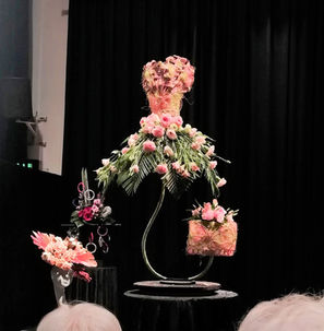 A 1950's style dress made out of flowers and foliage displayed on a stage with a matching floral bag