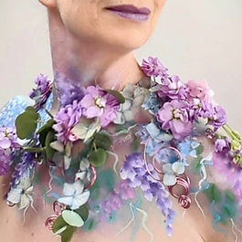 A lady with purple and turquoise flowers and painted flowers on her neck and shoulders