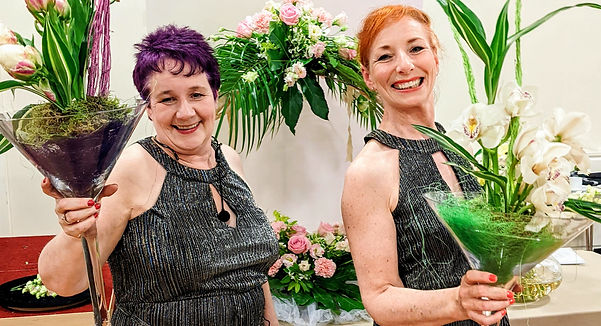 Two ladies holding glass cocktail vases with flower arrangements in them
