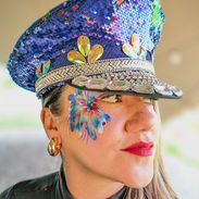 Lady wearing a blue sparkly cap with a glitter face art design around her eye