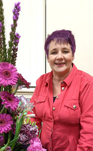 Lady in a pink boiler suit standing next to purple flowers