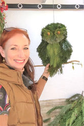 Lady standing next to an owl made from different green foliage 