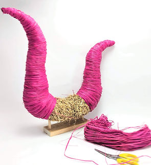 Straw sculpture wrapped in bright pink rafia, with a bunch of rafia next to it and pair of yellow scissors