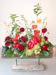 Red and orange flowers and red peppers arranged in a log container