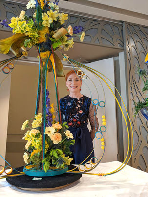 Lady waering blue standing next to a blue and yellow floral display