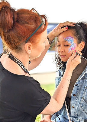 Lady painting and purple and blue eye design on the side of a childs facea childs