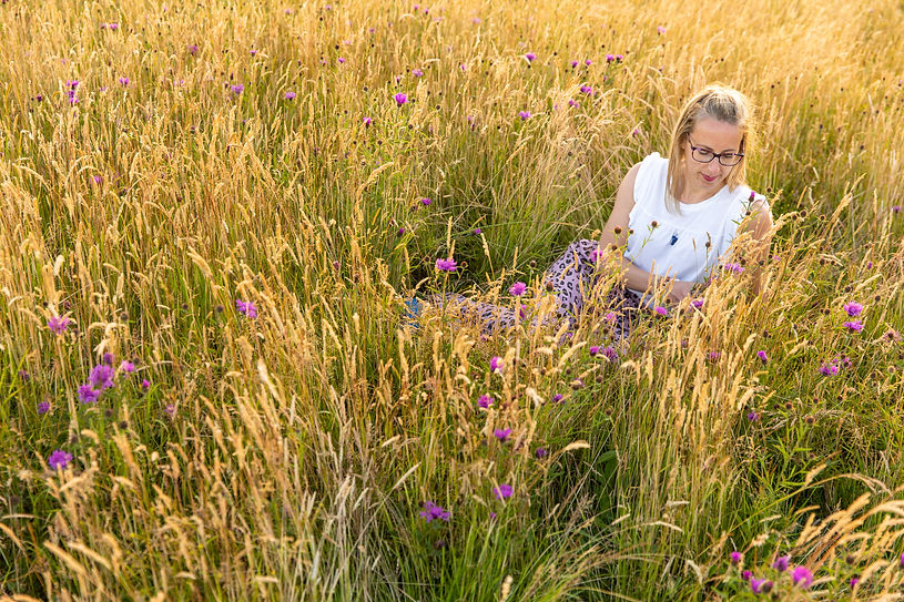 Abi sitting in a lavendar fiels wearing a white t-shirt, she is looking a the lavendar and smiling
