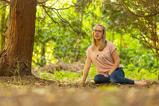 Abi Fenton wearing a t-shirt and jeans resting casually in the woods whilst looking at the camera