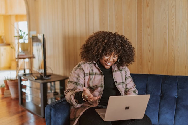 happy woman sitting down on couch looking at laptop