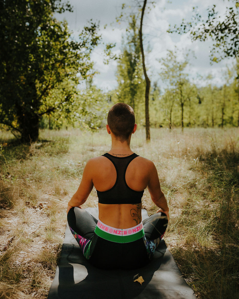 A person with a shaved head sits cross-legged on a yoga mat in a sunlit forest, facing away, in meditation—symbolizing nervous system regulation, inner stillness, and connection with nature.