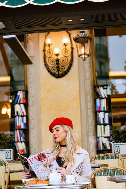 Modelo com boina vermelha lendo revista em café parisiense em Saint-Germain-des-Prés