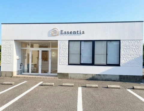 Essentiaのロゴ付きの白い建物と駐車スペース。窓と玄関。晴れた日の青い空。