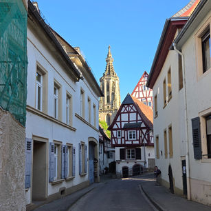 Weg durch eine Gasse zu einem Fachwerkhaus mit Blick auf eine Kirche hinter blauem Himmel